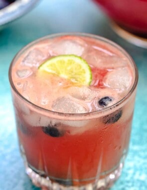 one glass of watermelon sangria, with ice, lime, and blueberries.