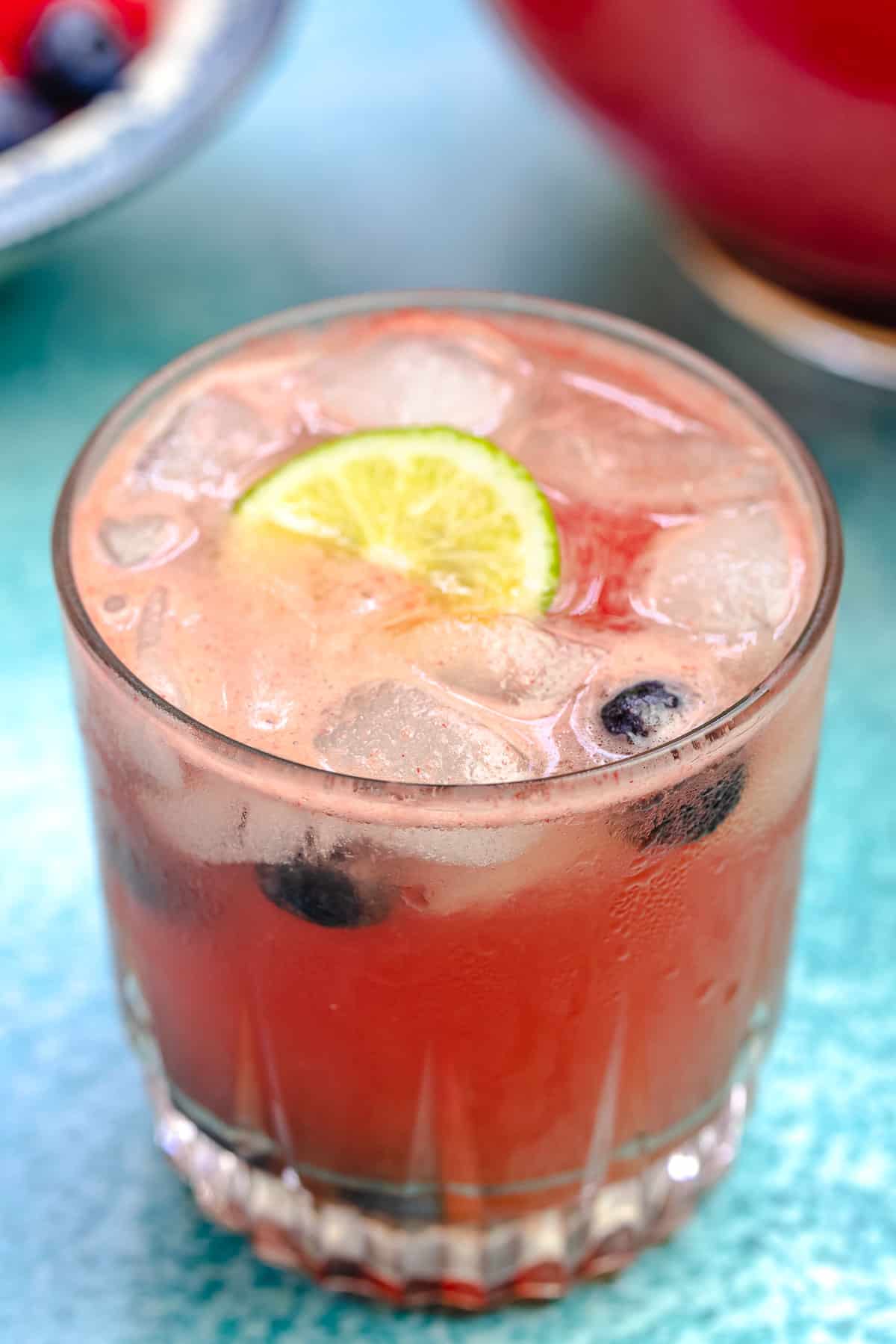 one glass of watermelon sangria, with ice, lime, and blueberries.