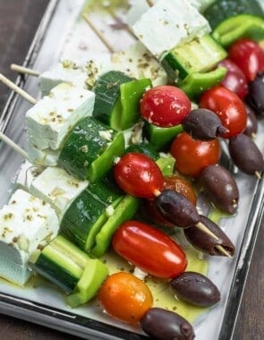 Greek salad kabobs on wooden skewers with a Greek-style vinaigrette drizzled over.