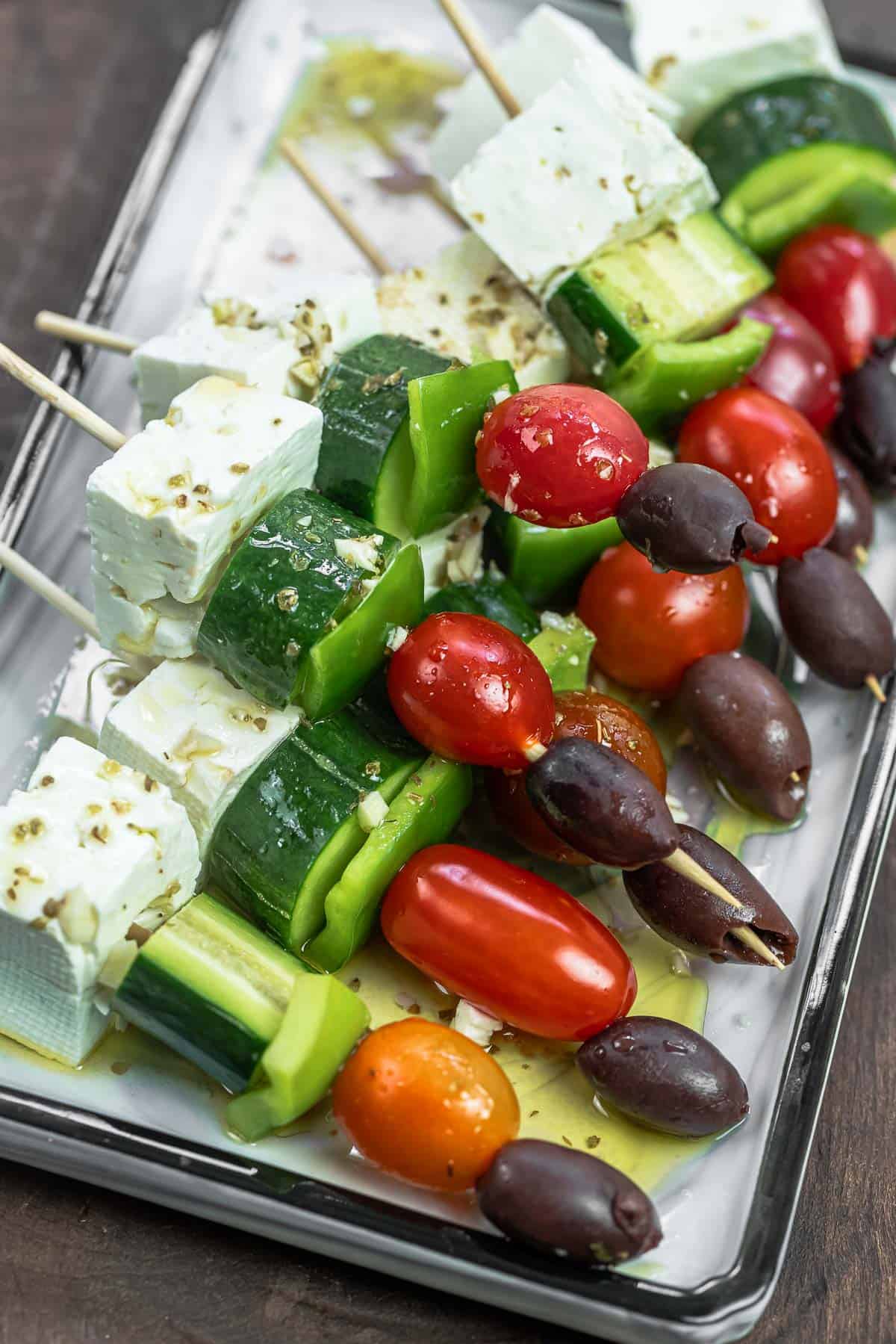 Greek salad kabobs on wooden skewers with a Greek-style vinaigrette drizzled over.