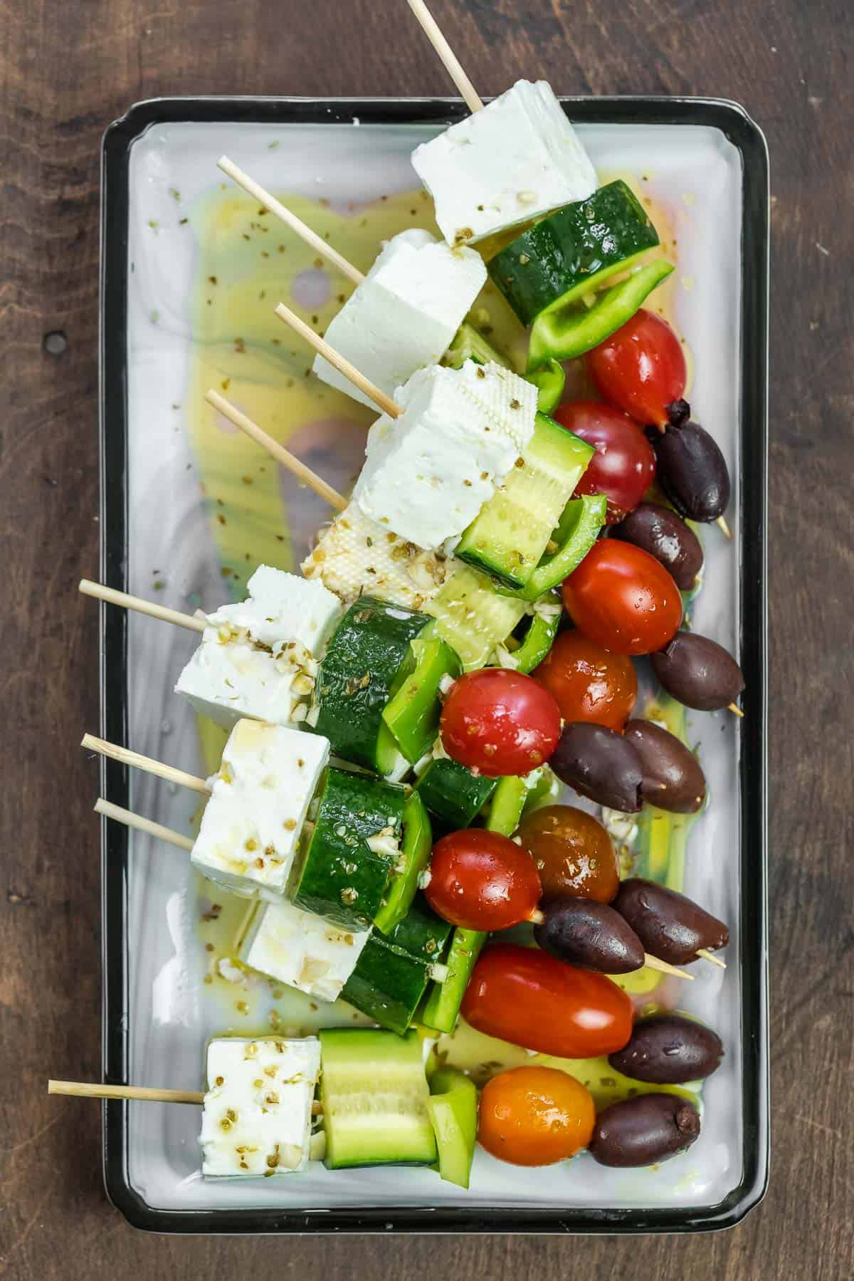 Greek salad skewers on a platter with homemade vinaigrette drizzled on top.