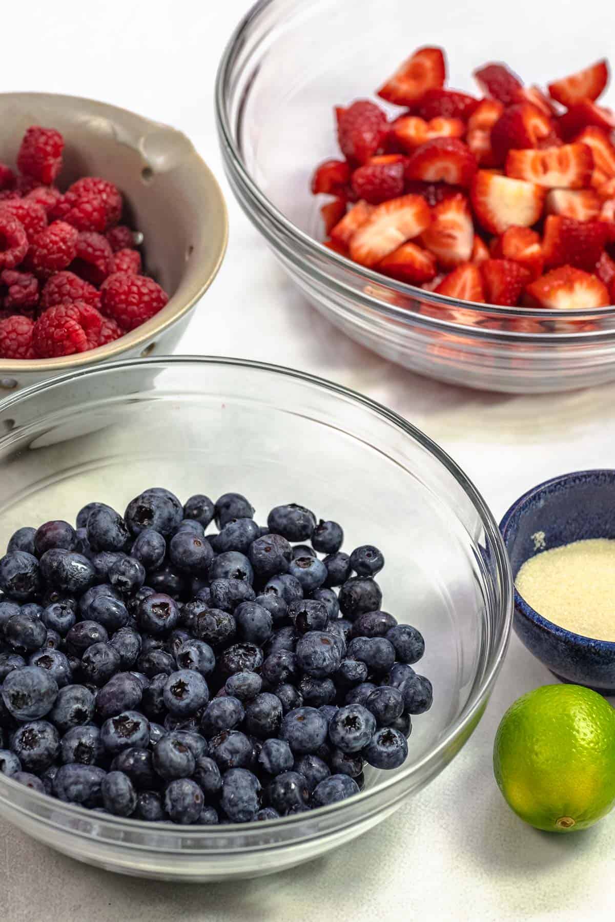 ingredients for berry compote including blueberries, raspberries, strawberries, lime, and sugar.