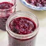 a jar filled with summer berry compote, with another filled jar and filled bowl in the background.