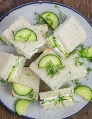 cucumber sandwich squares topped with a garnish of dill and sliced cucumber on a plate.