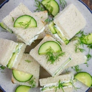 cucumber sandwich squares topped with a garnish of dill and sliced cucumber on a plate.