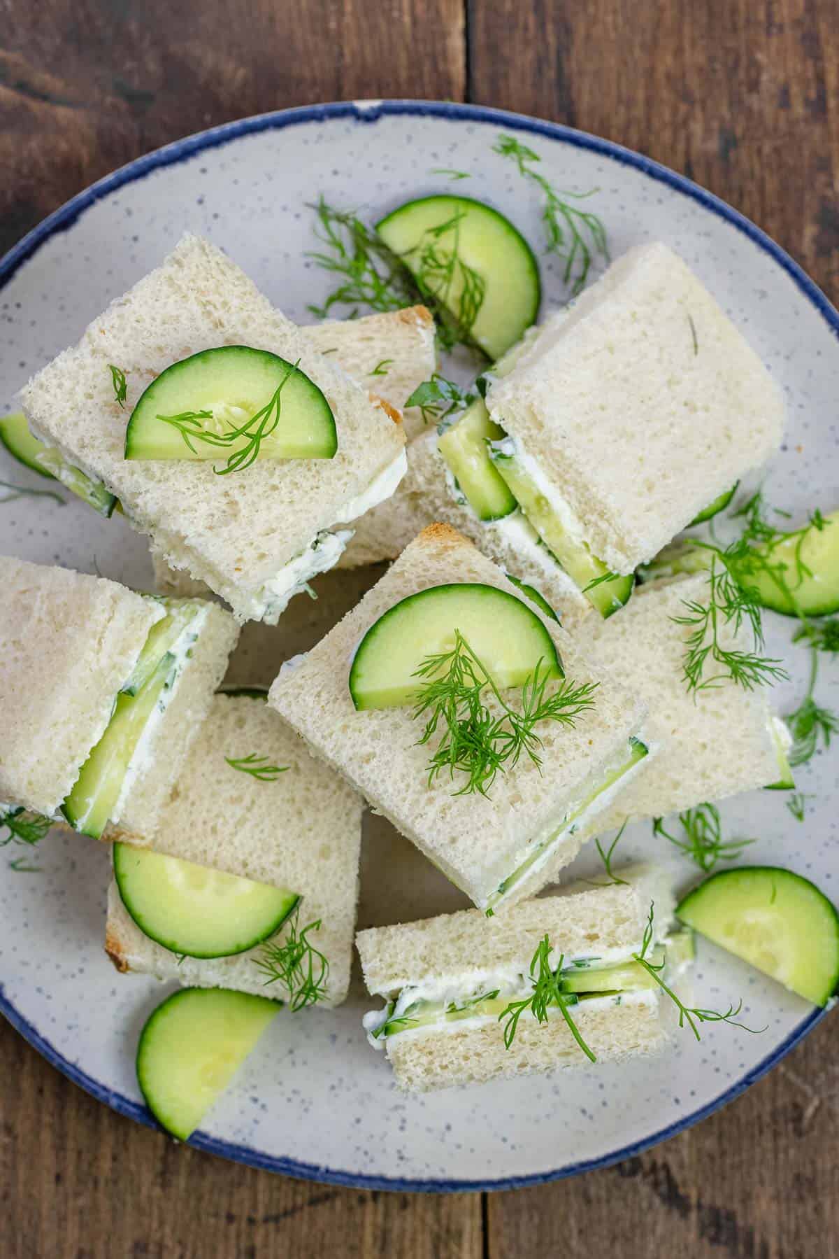 cucumber sandwich squares topped with a garnish of dill and sliced cucumber on a plate.