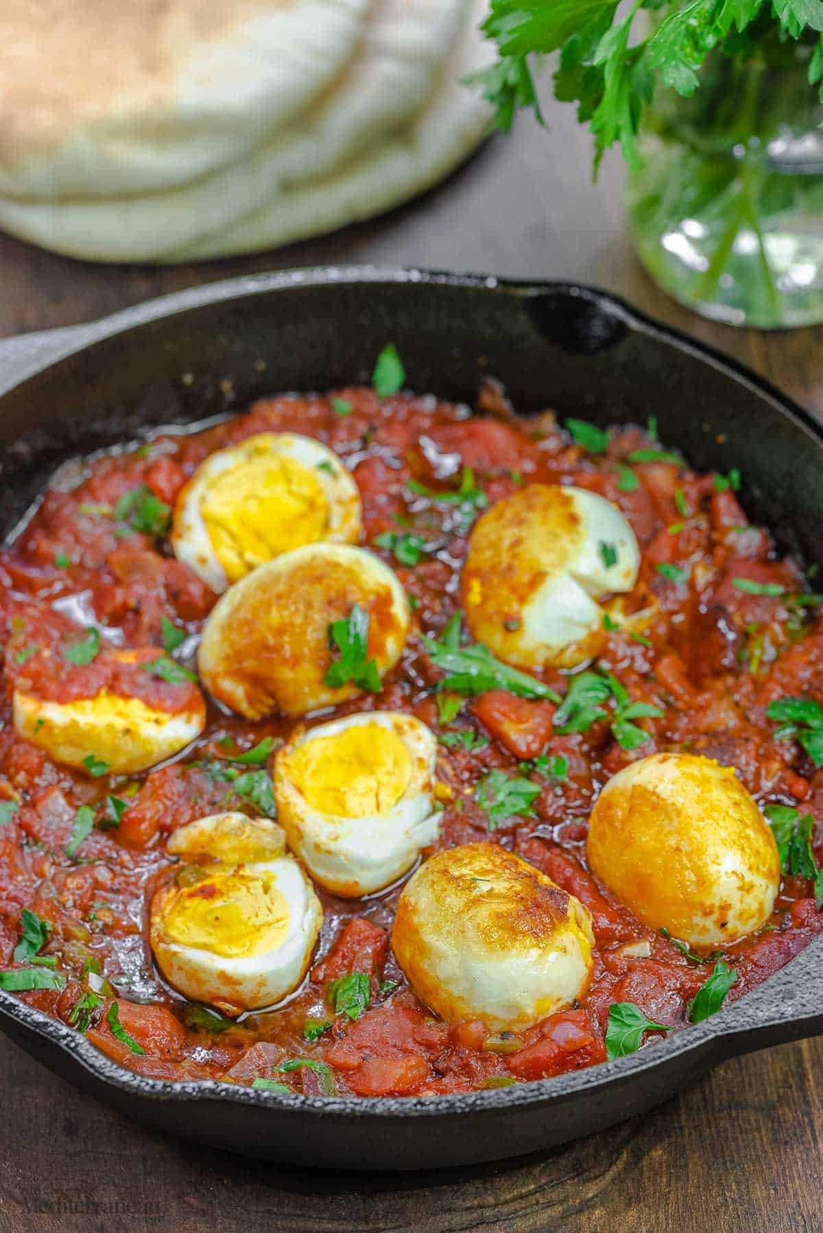 œufs dans une sauce tomate italienne épicée avec une pile de pain pita et quelques herbes à côté