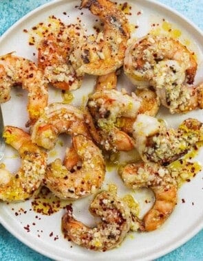 grilled jumbo shrimp with sauce and Parmesan cheese on a white plate with lemon halves in the background.