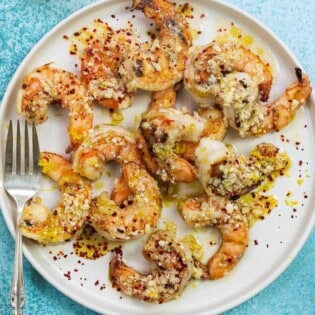 grilled jumbo shrimp with sauce and Parmesan cheese on a white plate with lemon halves in the background.