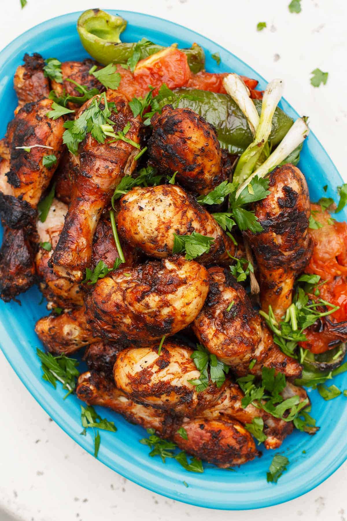 grilled chicken legs on a blue serving platter with charred bell peppers and fresh herbs.