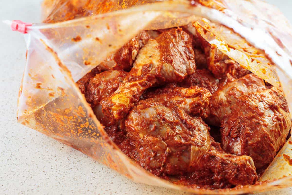uncooked chicken legs in a Ziploc bag with harissa marinade.