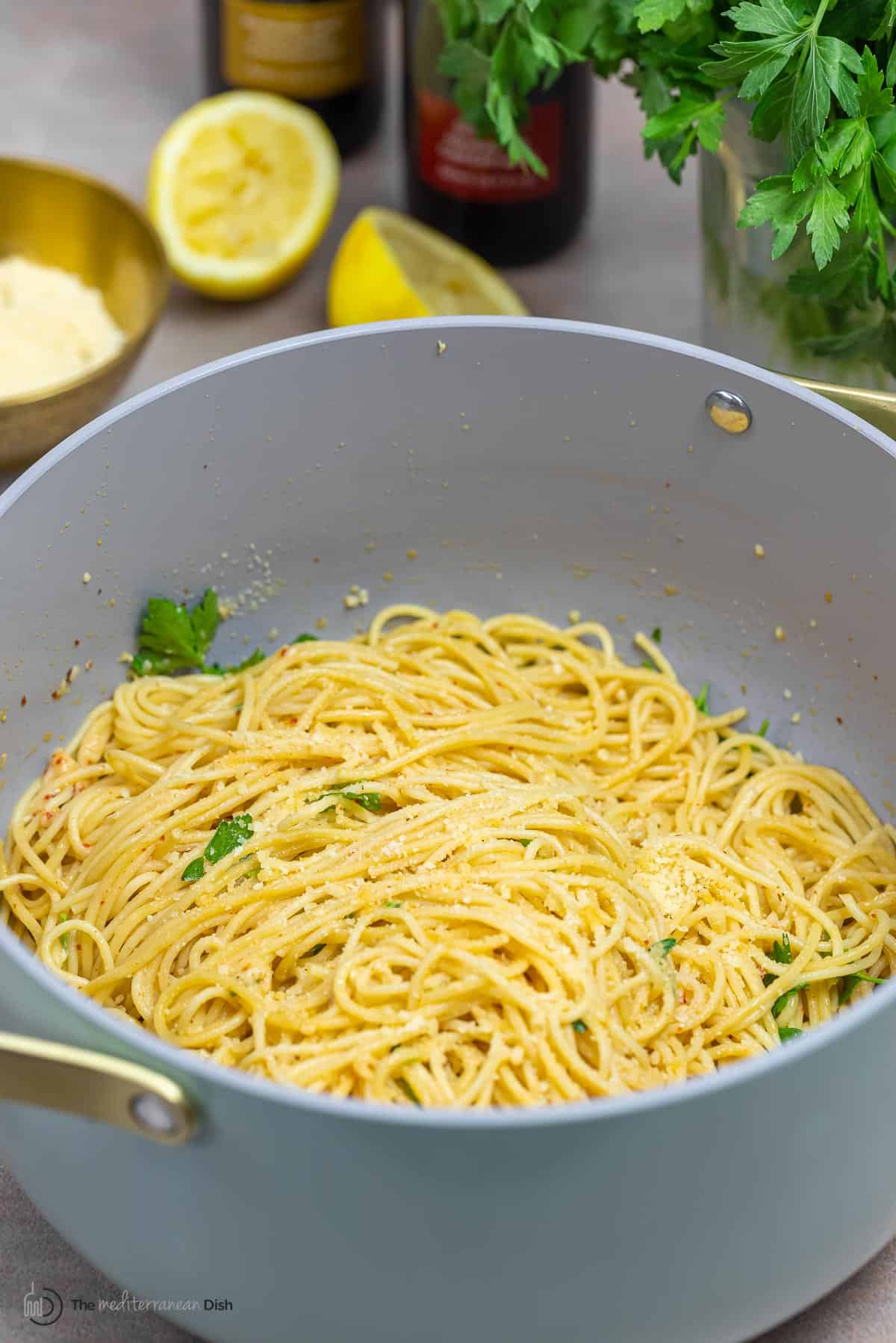 lemon pasta in a pot with lemon, parmesan cheese, olive oil, and fresh parsley in the background.