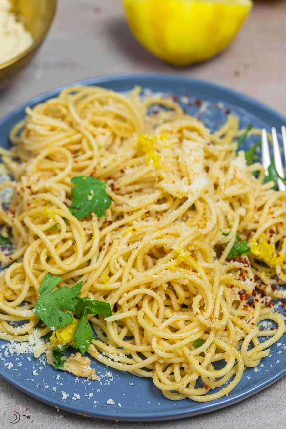 a lighter spaghetti al limone on a plate sprinkled with parmesan cheese and red pepper flakes.