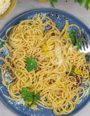 lemon pasta on a plate with a garnish of fresh parsley and a sprinkle of parmesan cheese, red pepper flakes, and lemon zest.