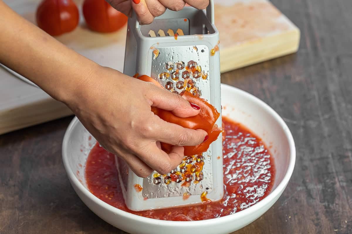 Tomatoes being grated with a box grater into a bowl.