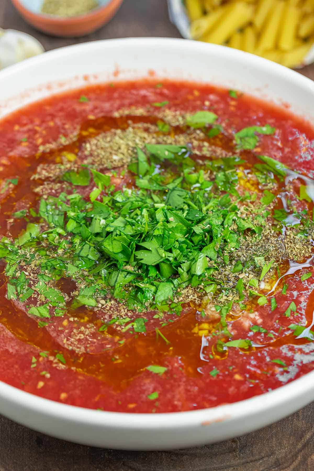 pomodoro crudo (no-cook tomato sauce) in a bowl sprinkled with fresh chopped parsley. A side of penne pasta just next to it. 