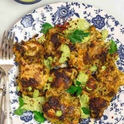 green goddess chicken thighs on a blue and white plate, with green goddess sauce drizzled over.