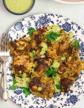 green goddess chicken thighs on a blue and white plate, with green goddess sauce drizzled over.