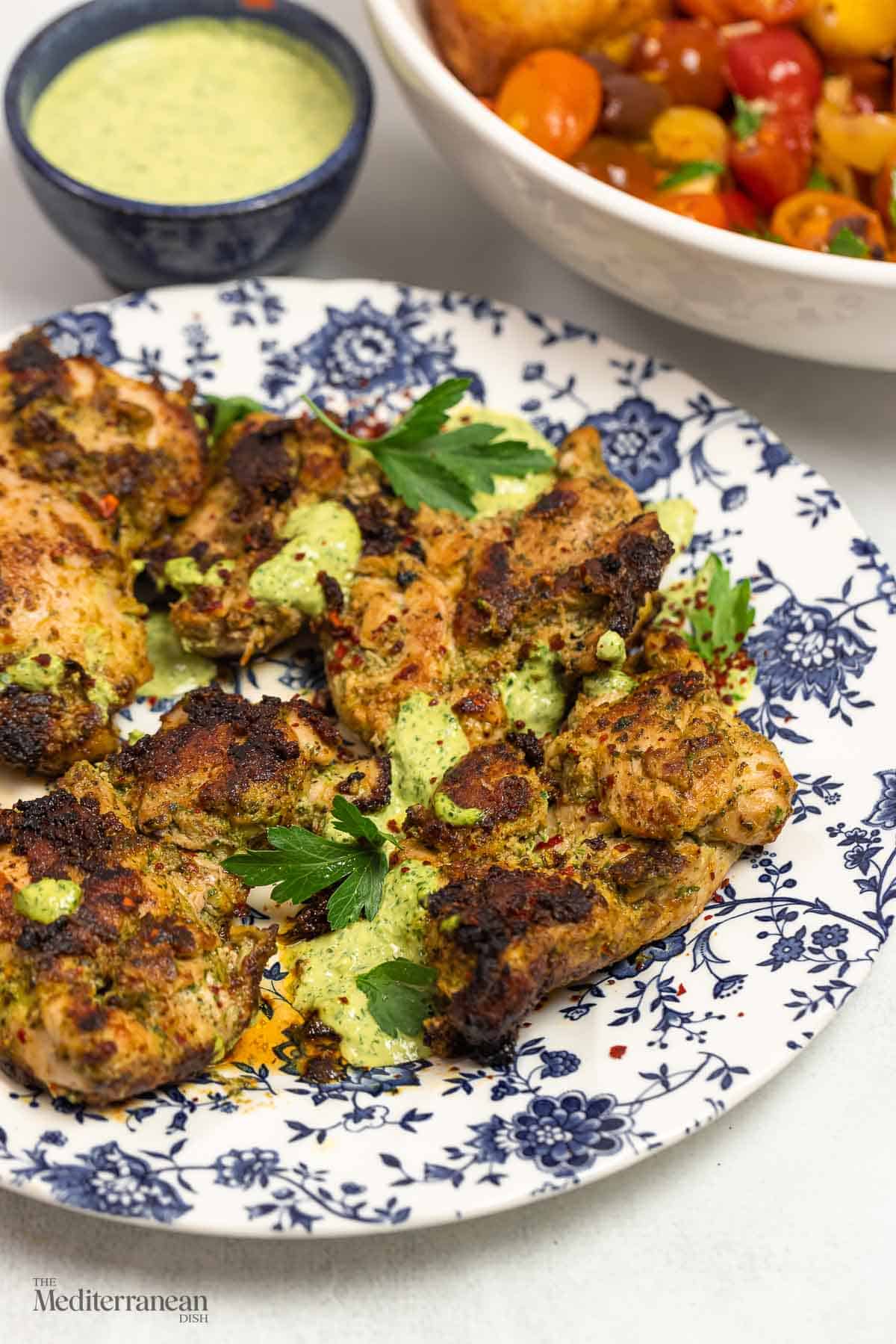 green goddess chicken on a plate, with extra green goddess sauce for dipping in the background.