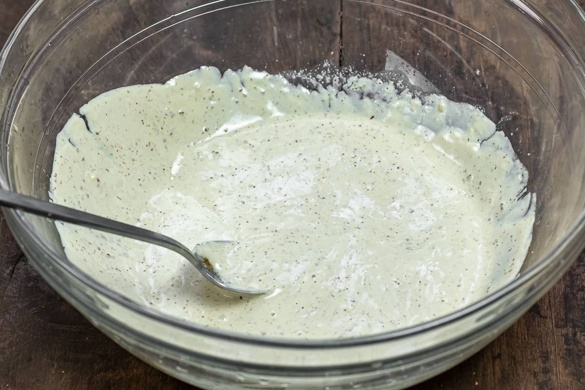 prepared cold noodle salad dressing in a mixing bowl with a spoon.