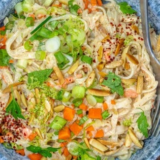 noodle salad with vegetables and slivered nuts in a blue bowl with a fork.