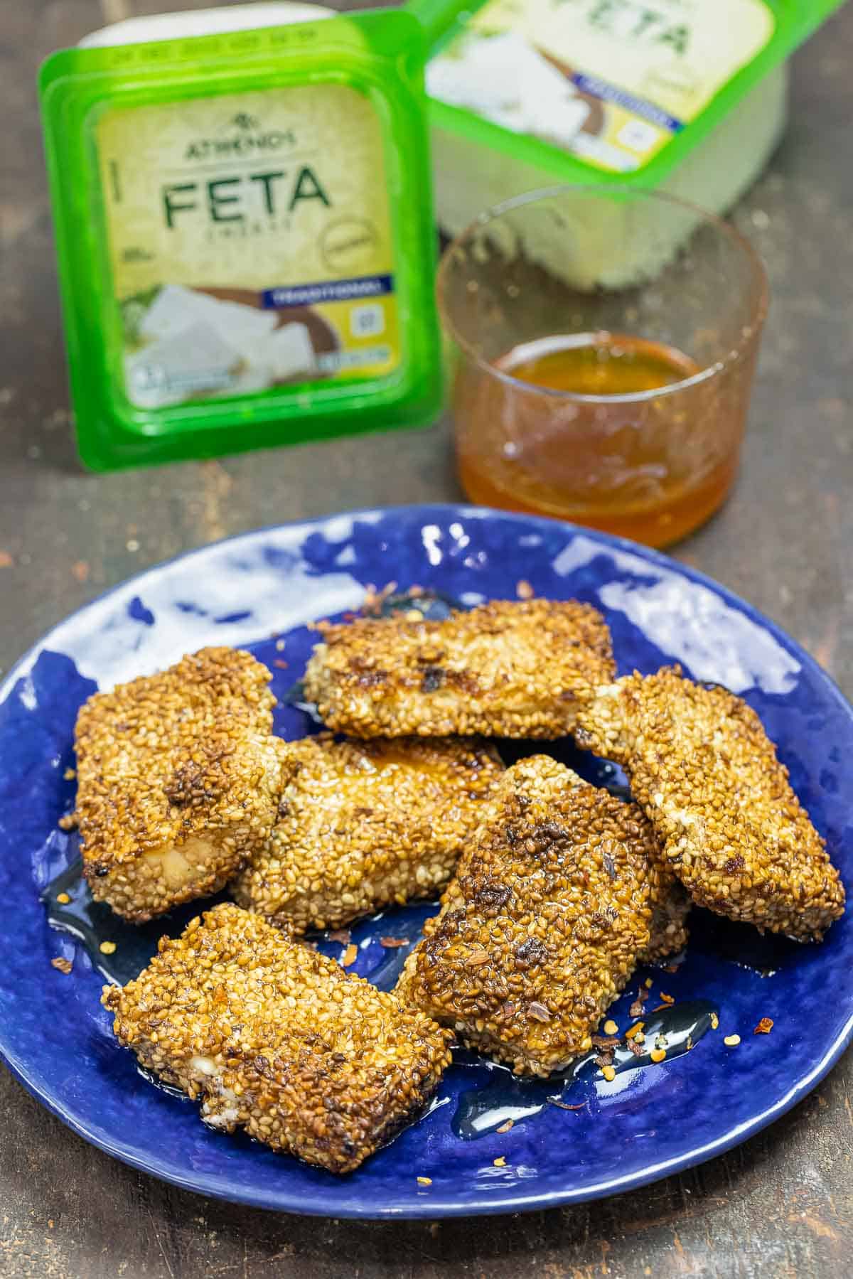 fried feta cheese on a plate with a container of feta cheese and a bowl of honey in the background.