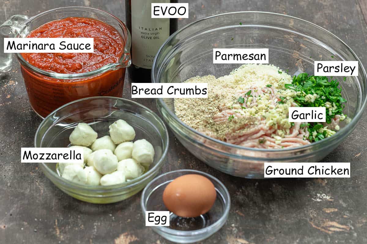 labeled ingredients for stuffed meatballs including marinara sauce, olive oil, baby mozzarella, egg, ground chicken, bread crumbs, garlic, parsley, and parmesan cheese.