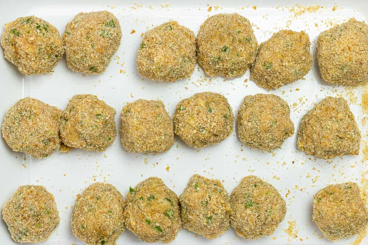 chicken meatballs with mozzarella coated in bread crumbs and placed on a baking sheet.