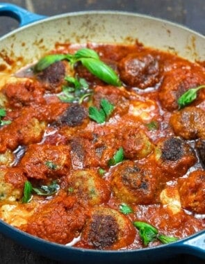 cheese stuffed meatballs in a large skillet with marinara sauce and some fresh basil on top.