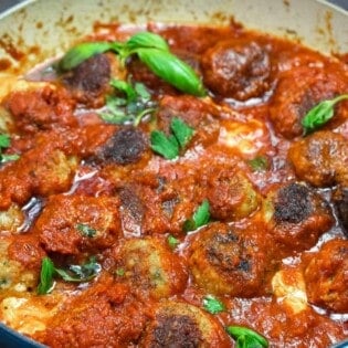 cheese stuffed meatballs in a large skillet with marinara sauce and some fresh basil on top.