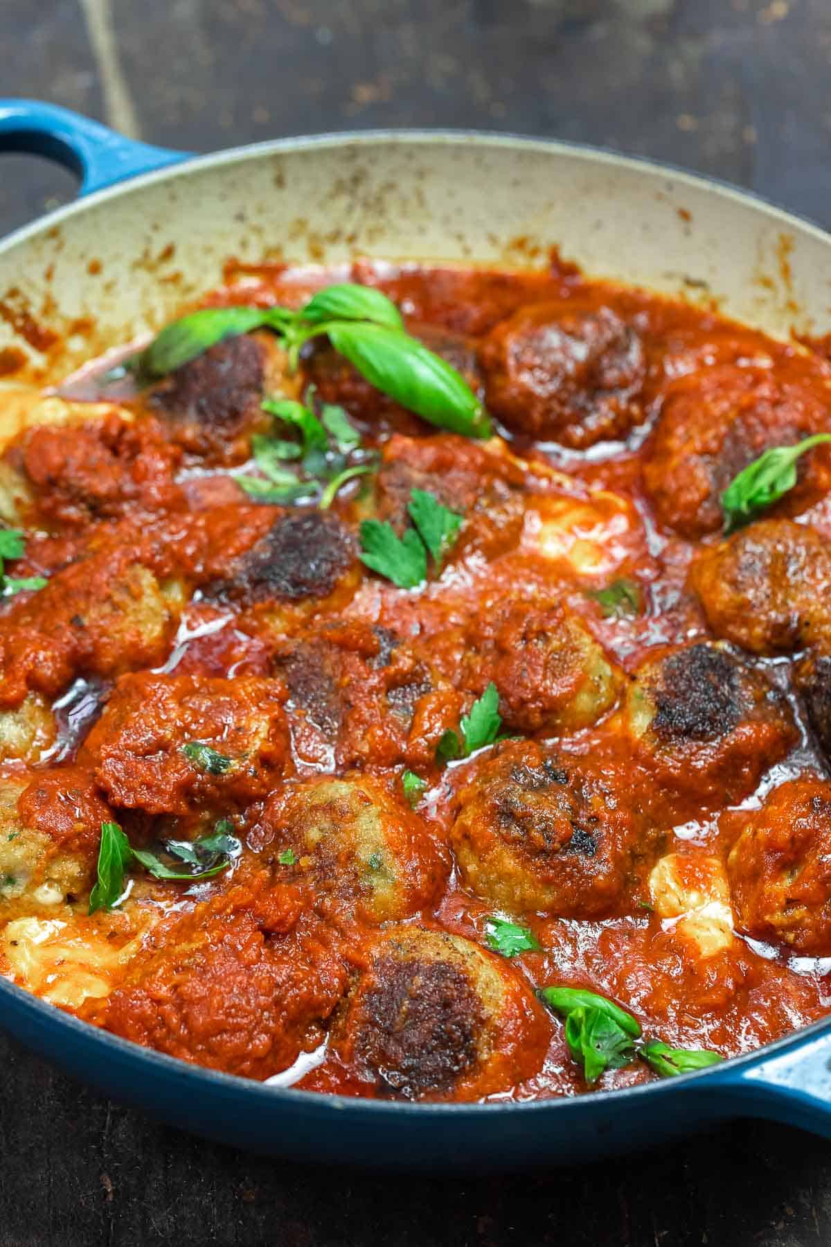 cheese stuffed meatballs in a large skillet with marinara sauce and some fresh basil on top.