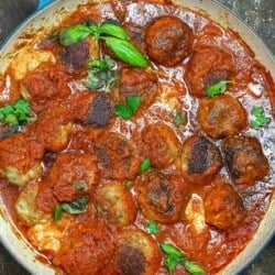 chicken parmesan meatballs in a skillet with tomato sauce and fresh basil.