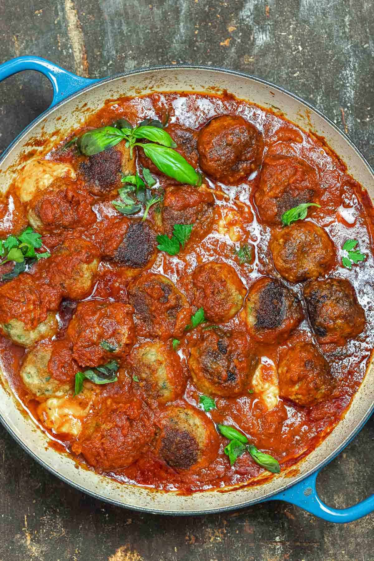chicken parmesan meatballs in a skillet with tomato sauce and fresh basil.