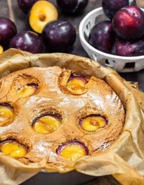 plum cake in a cake tin with fresh plums in the background.