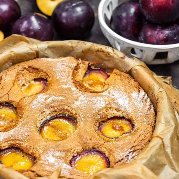plum cake in a cake tin with fresh plums in the background.
