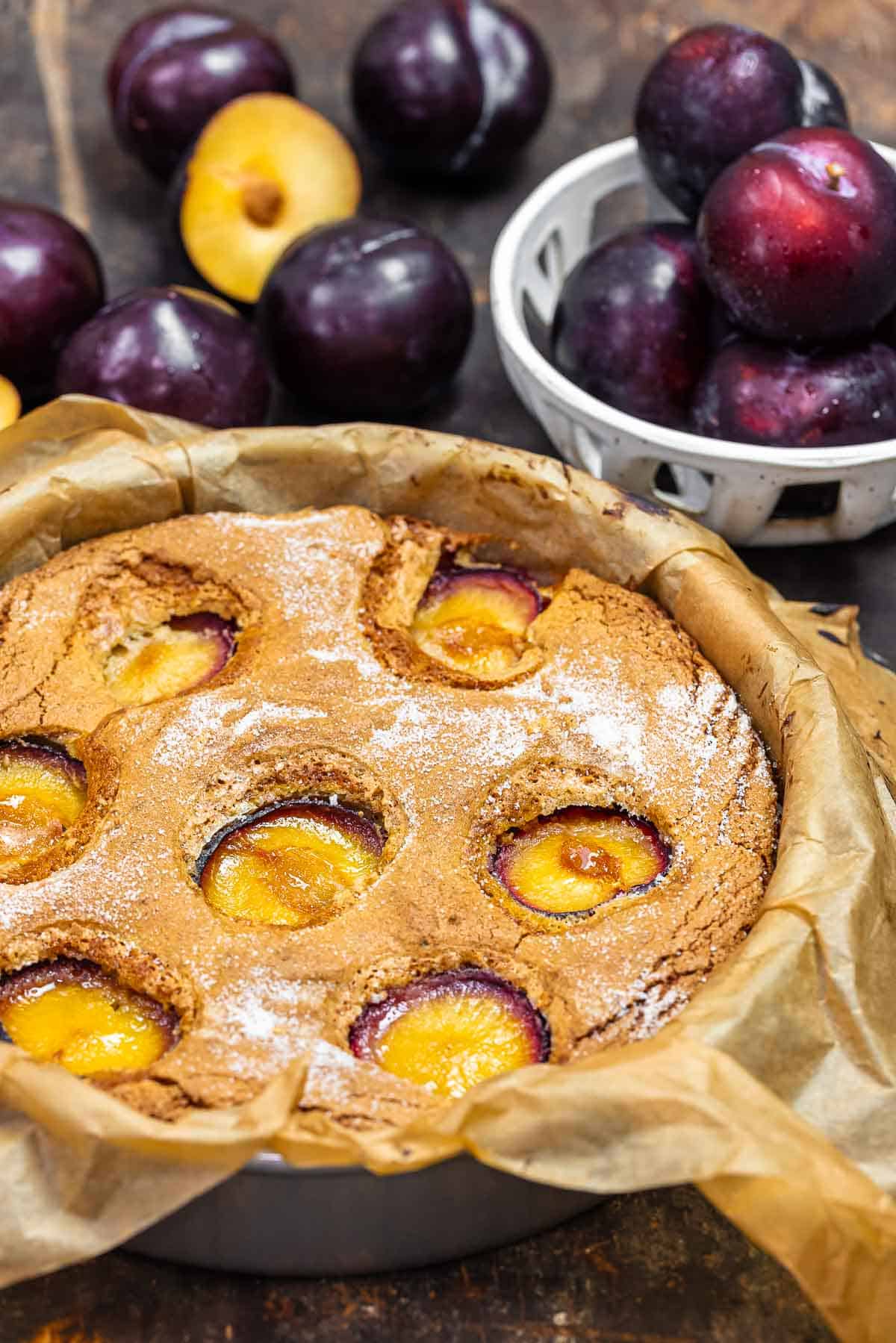 plum cake in a cake tin with fresh plums in the background.