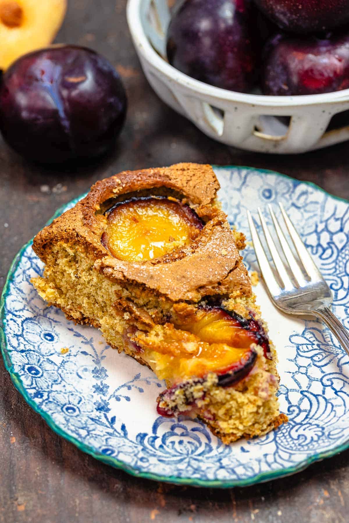 slice of fresh plum cake on a blue and white plate with a fork.