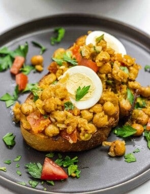 chickpeas on toast with eggs on top on a dark plate.