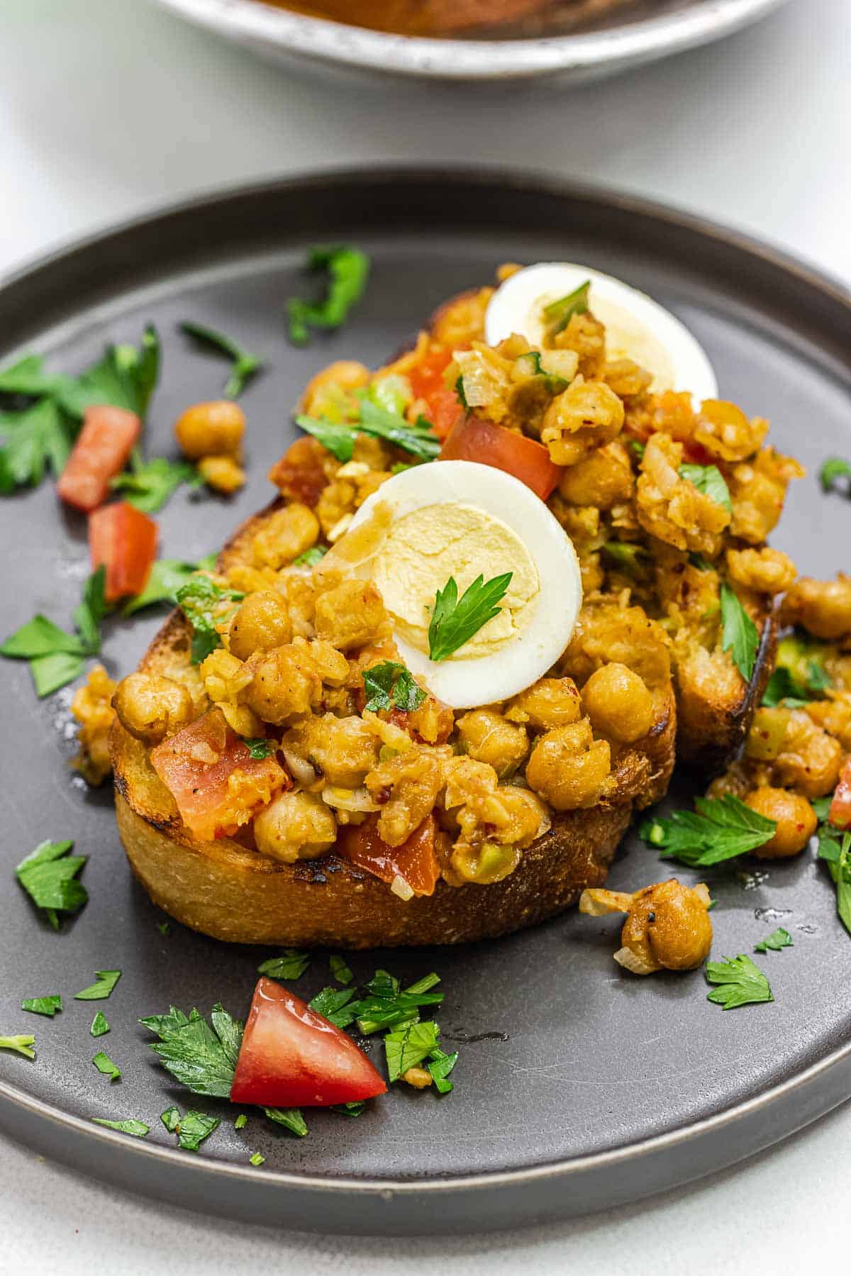 chickpeas on toast with eggs on top on a dark plate.