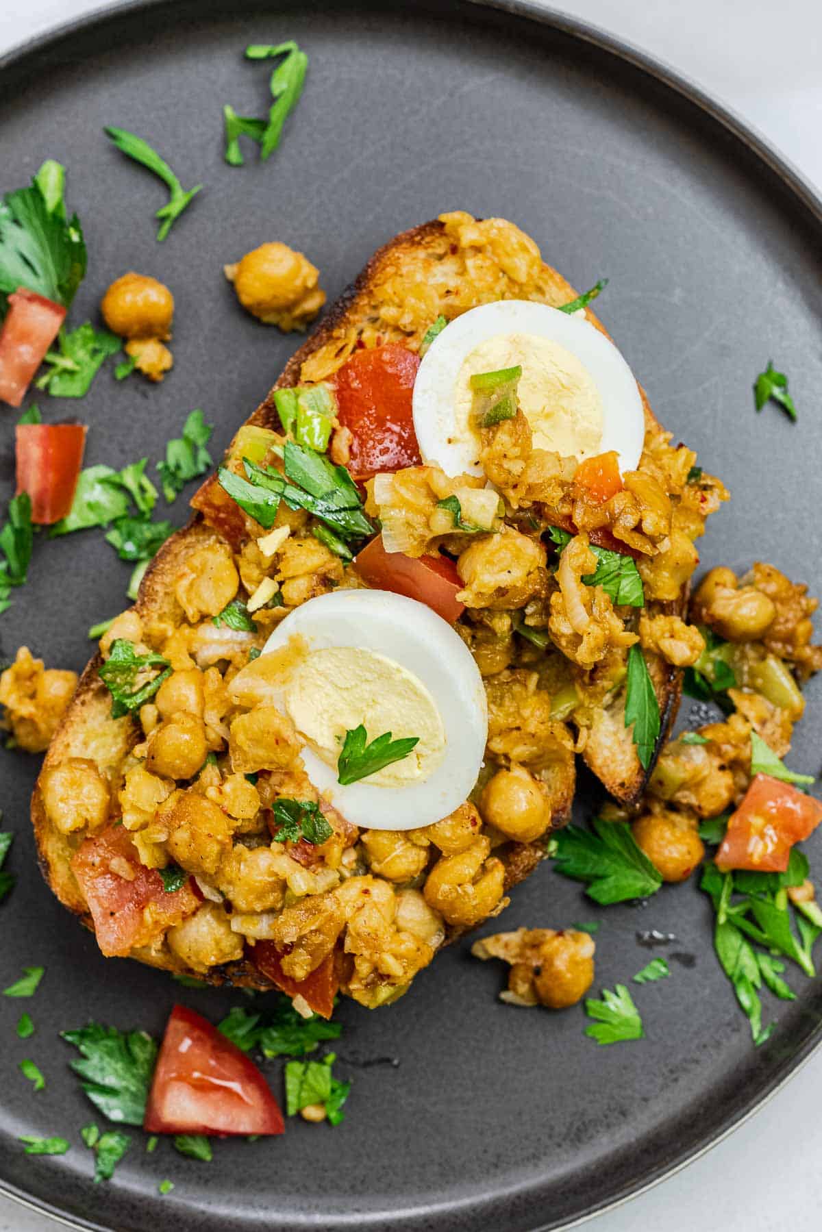 vegetarian smashed chickpea toast on a plate topped with fresh parsley.