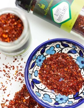 Image of Aleppo pepper flakes with two bottles of them, as well as some in a small blue and white bowl.