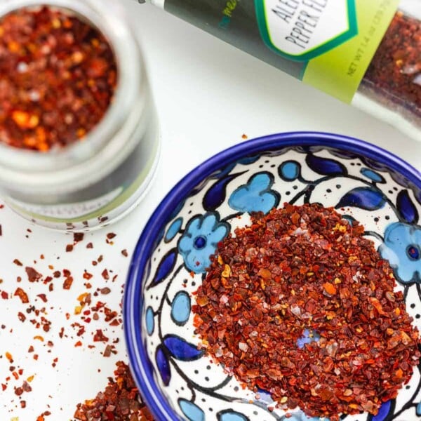 Image of Aleppo pepper flakes with two bottles of them, as well as some in a small blue and white bowl.