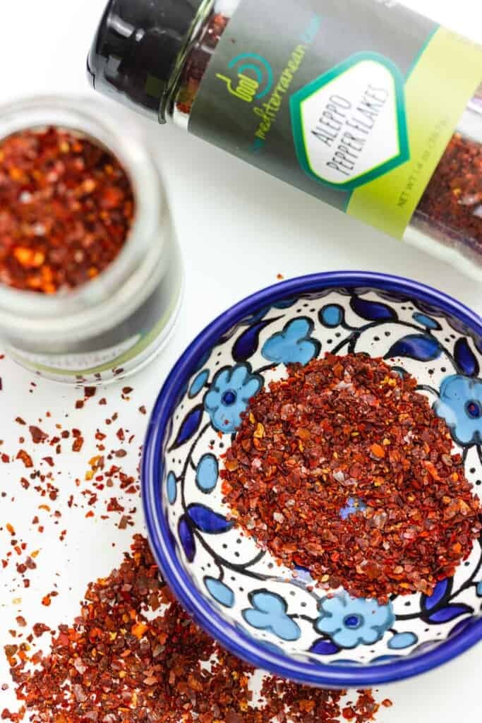 Image of Aleppo pepper flakes with two bottles of them, as well as some in a small blue and white bowl.