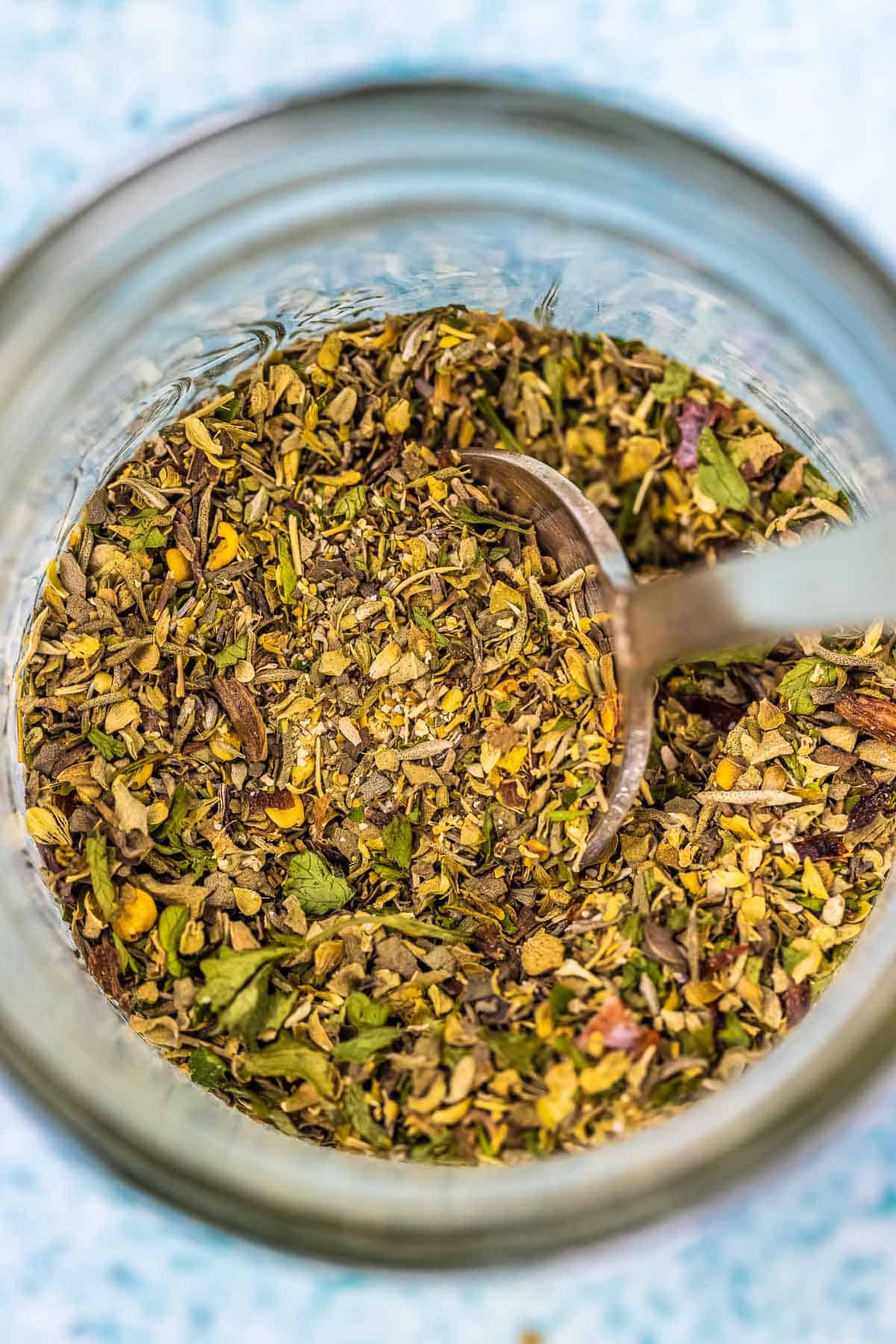 Close up of Italian seasoning in a jar with a spoon.