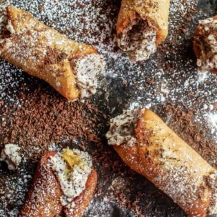 several cannoli dusted with powdered sugar and finished with grated chocolate.