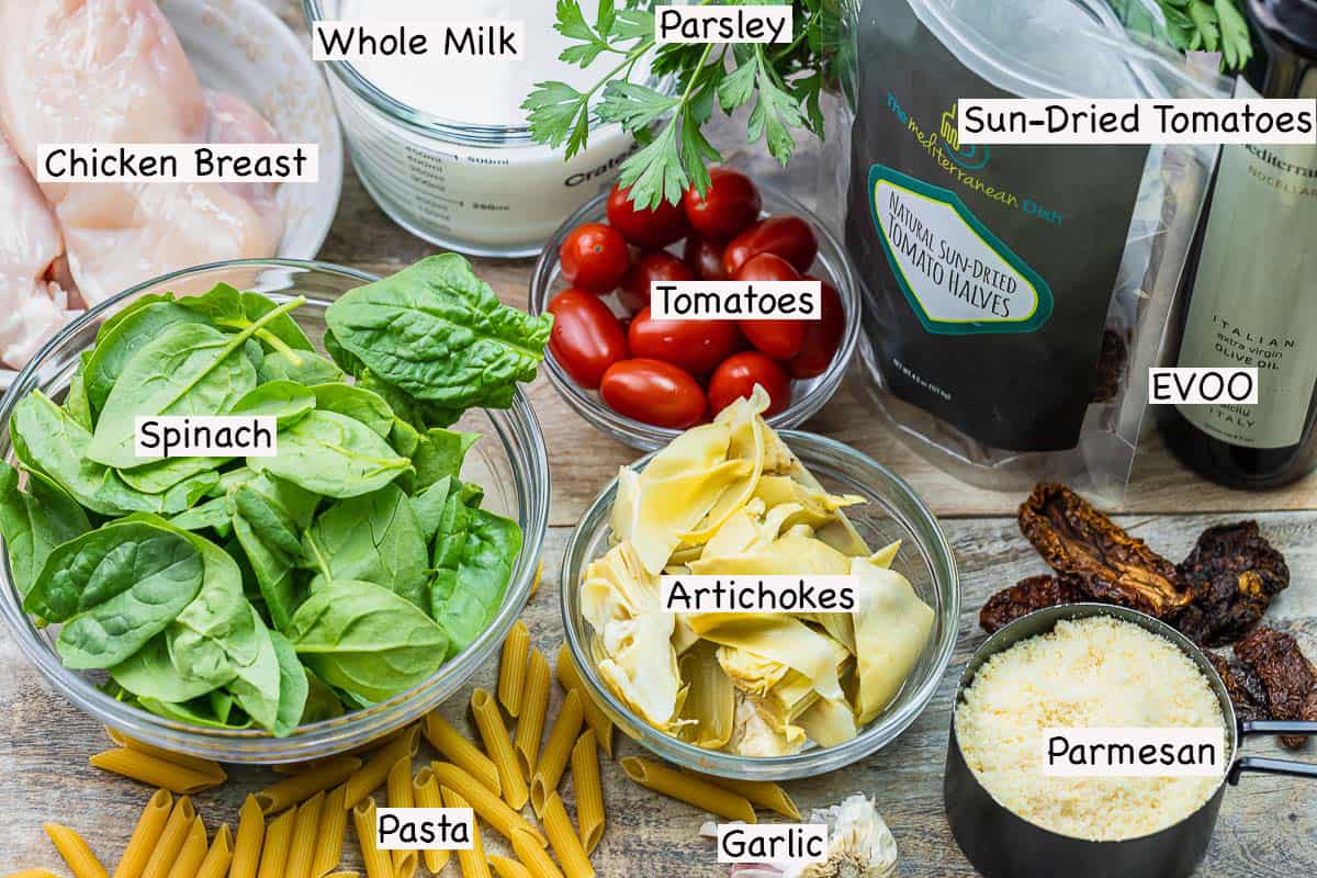 labeled ingredients for chicken pasta including olive oil, sun-dried tomatoes, parmesan cheese, artichokes, cherry tomatoes, whole milk, spinach, chicken breasts, parsley, and penne pasta.