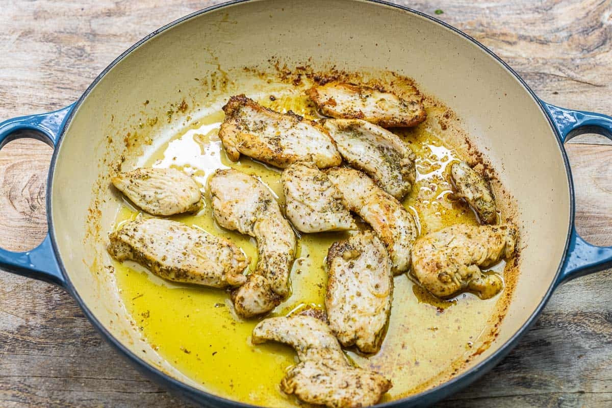 boneless skinless chicken breast slices cooking in olive oil in a pan.