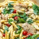 chicken pasta with spinach and cherry tomatoes in a pan.