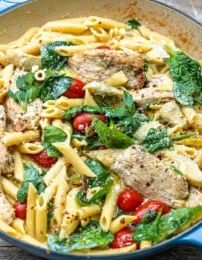 chicken pasta with spinach and cherry tomatoes in a pan.