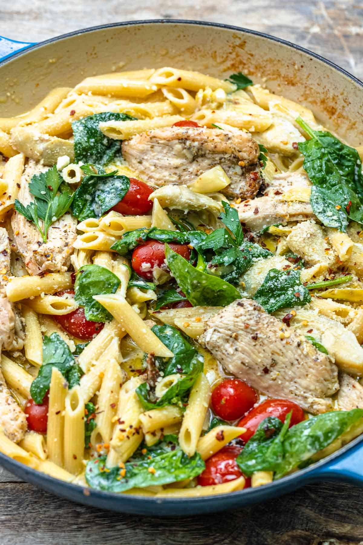 chicken pasta with spinach and cherry tomatoes in a pan.